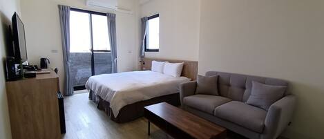 A hotel room with a bed, a sofa, a wooden coffee table, a desk with a computer and phone, and a TV.