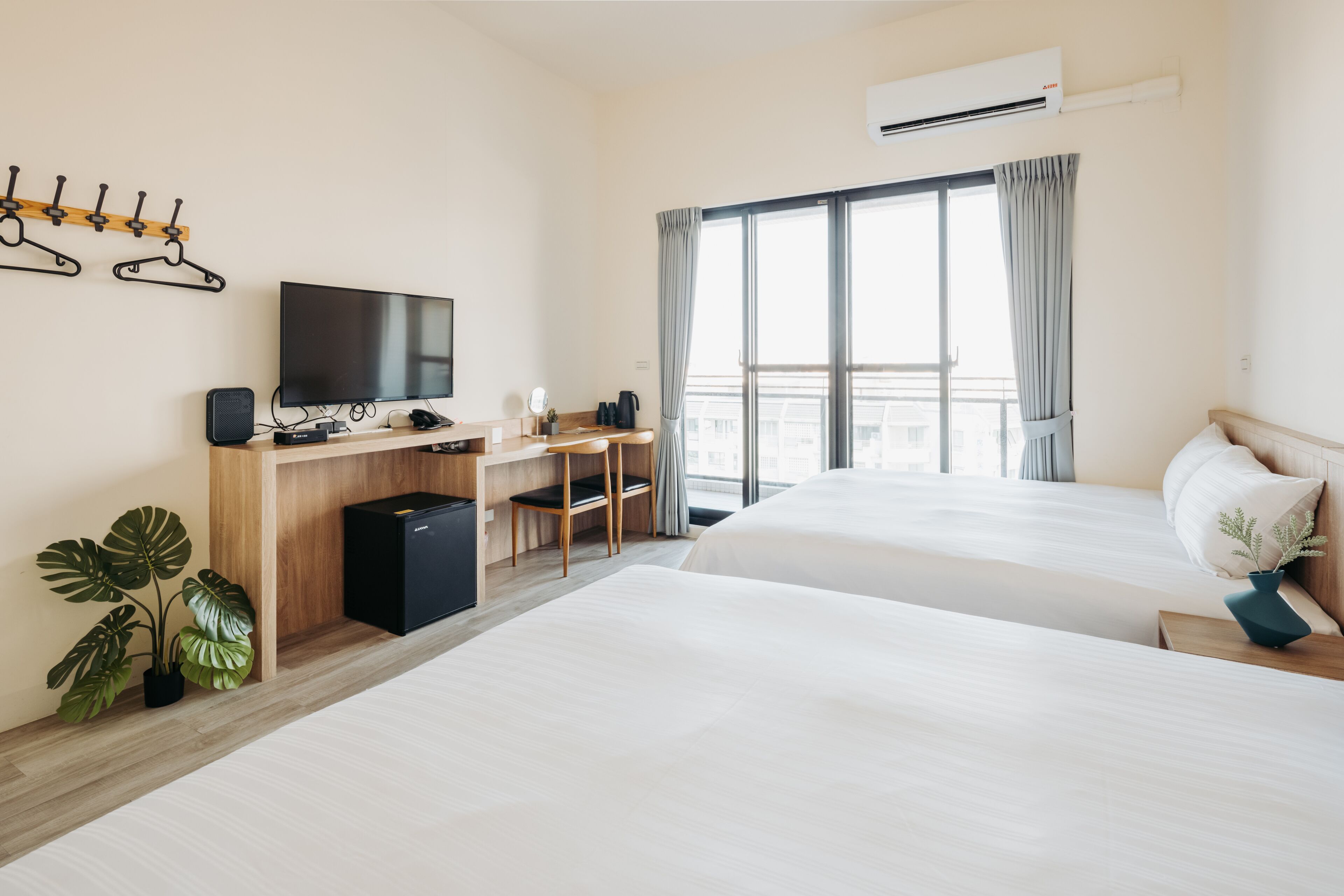 Habitación de hotel con dos camas, un escritorio con silla, televisión y un gran ventanal con cortinas.
