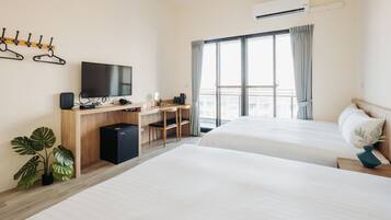 Habitación de hotel con dos camas, un escritorio con silla, televisión y un gran ventanal con cortinas.