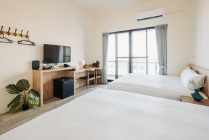 Habitación de hotel con dos camas, un escritorio con silla, televisión y un gran ventanal con cortinas.