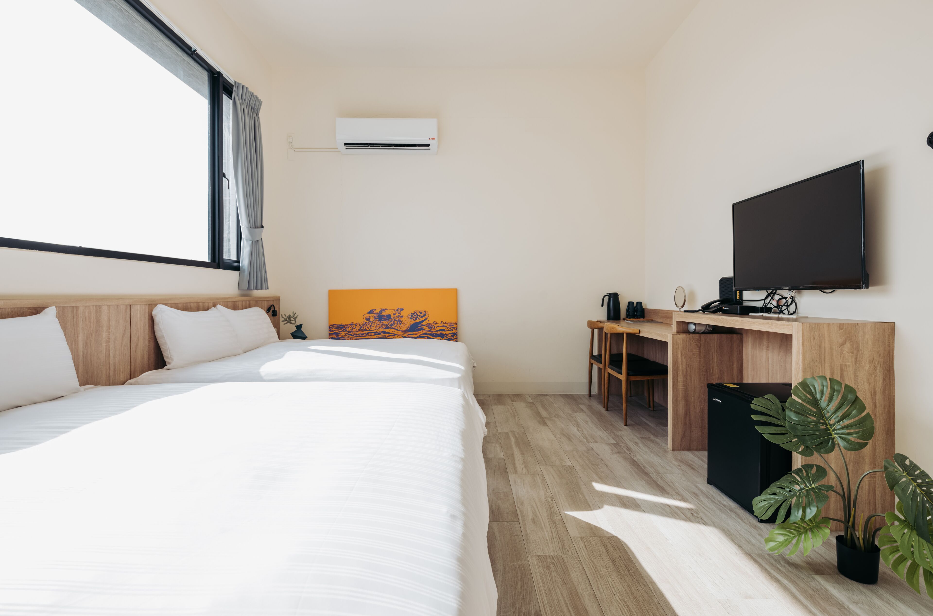 A hotel room with a large bed, a desk with a flat-screen TV, an air conditioner, and a potted plant.