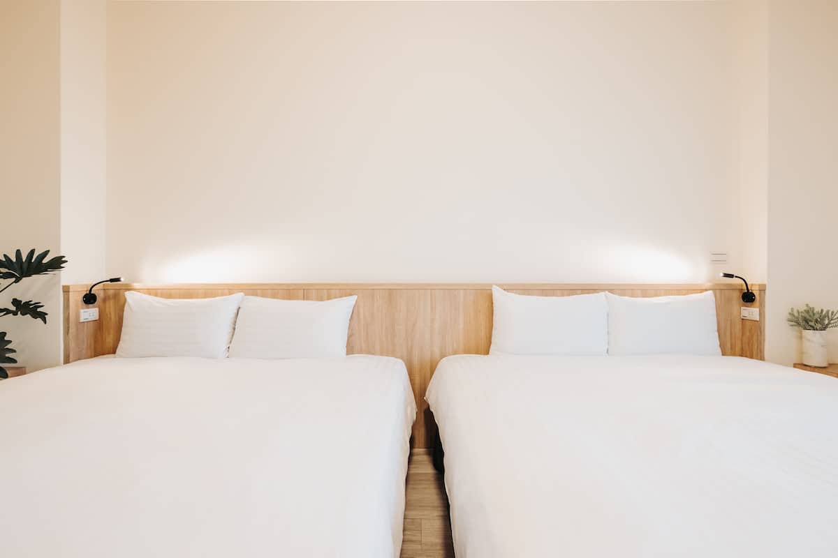Ein Hotelzimmer mit zwei Einzelbetten, Holz-Kopfteilen, weißer Bettwäsche und Nachttischlampen.