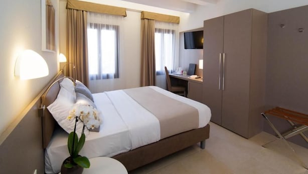 A hotel room with a bed, a desk, a TV, and a wardrobe. - Leone (Venice)