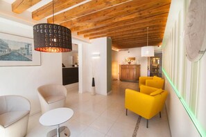 A modern interior with a wooden ceiling, a dining area with yellow chairs, and a kitchen in the background. - Leone (Venice)