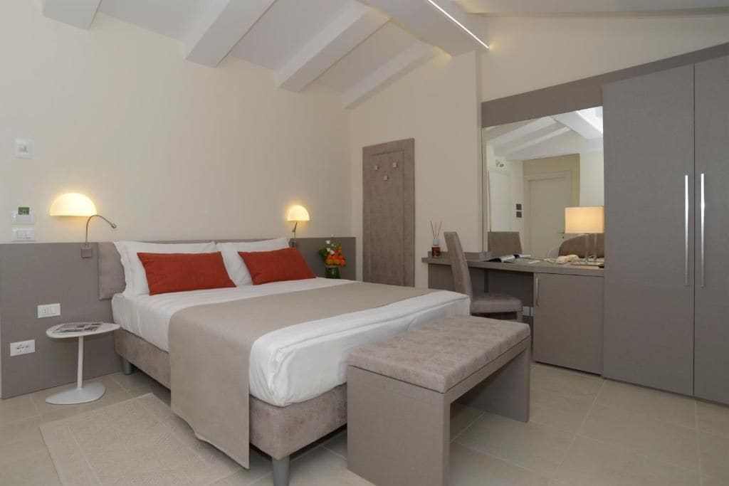 A modern hotel room with a bed, bedside tables, a desk, and a wardrobe.