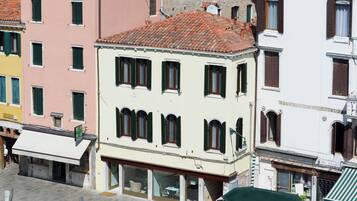 A multi-story building with a tiled roof, large windows with shutters, and a sign indicating a business on the ground floor.