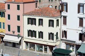 A multi-story building with a tiled roof, large windows with shutters, and a sign indicating a business on the ground floor. - Leone (Venice)
