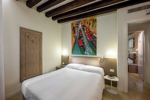 A hotel room with a bed, a painting of a canal, a nightstand, a bedside table, and a door leading to a bathroom. - Leone (Venice)