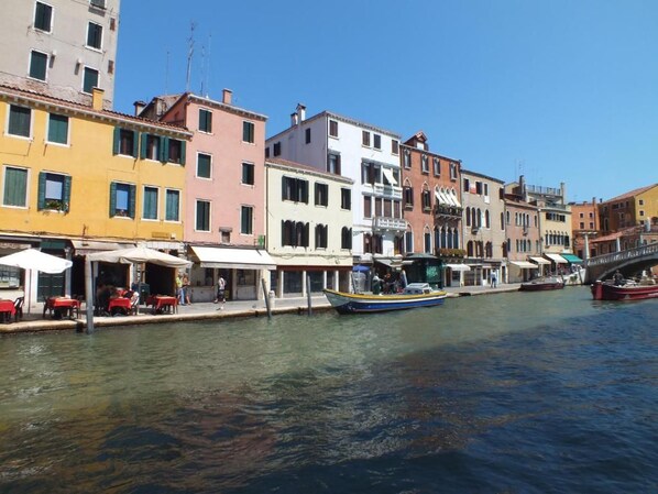 Un canal bordé de bâtiments aux couleurs vives, un bateau et des tables installées en plein air le long du quai.