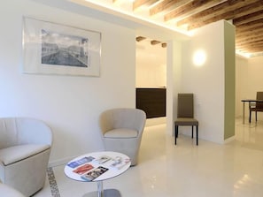 A modern hotel lobby with a minimalist design, featuring a round table with magazines, two armchairs, and a framed picture on the wall. - Leone (Venice)