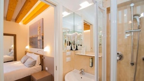 A modern hotel room with a bed, bedside table, and a bathroom with a sink and shower. - Leone (Venice)