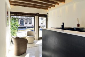 A modern interior with a reception desk, seating area, and large windows offering a view of the street. - Leone (Venice)