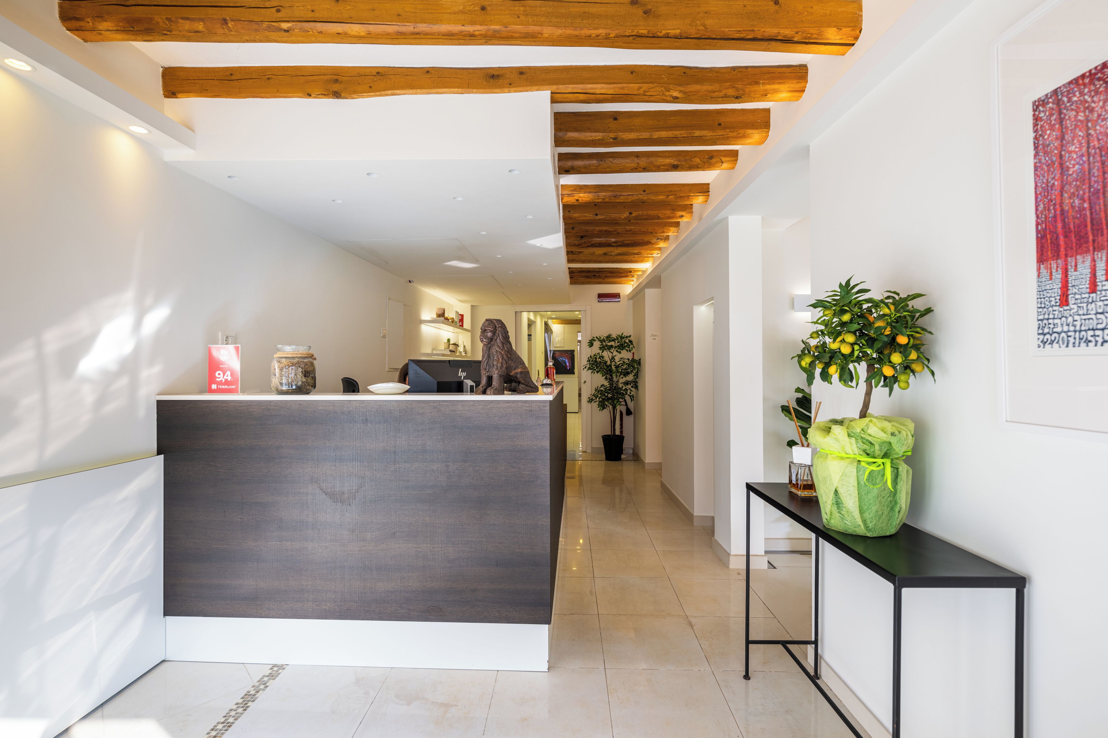 A reception area with a modern desk, wooden ceiling beams, a potted plant, and a framed artwork on the wall.