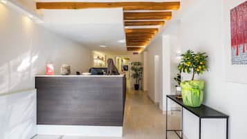 A reception area with a modern desk, wooden ceiling beams, a potted plant, and a framed artwork on the wall.