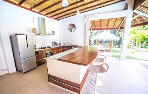 Une cuisine moderne dotée d’un îlot central, d’appareils électroménagers en acier inoxydable et offrant une vue sur l’extérieur.