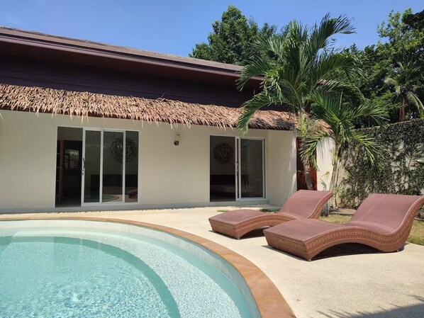 Un espace aménagé au bord de la piscine, avec des chaises longues et un bâtiment dont le toit est fait de chaume.