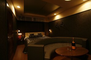 Una habitación de hotel moderna con una cama curva, una mesa redonda de madera y una botella de champán.