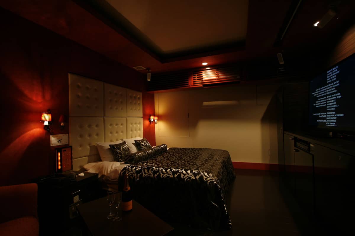 A hotel room with a large bed, a TV, and a desk with a lamp.