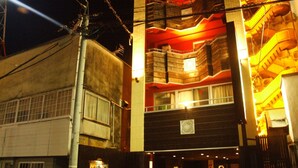 Um edifício de vários andares com estilo arquitetônico tradicional, com varandas de madeira e uma entrada central com um pequeno santuário.