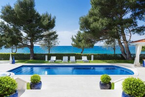 Ein Swimmingpool mit Liegestühlen und Topfpflanzen mit Blick auf ein klares, blaues Meer.
