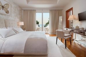 Ein geräumiges Schlafzimmer mit einem großen Bett, einem Schreibtisch, einem Stuhl, einem Fernseher und einem Balkon mit Meerblick.