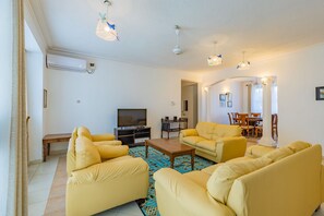 A living room with yellow sofas, a wooden coffee table, a flat-screen TV, and a patterned rug.