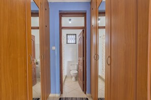 A hallway with wooden doors leading to a bathroom with a toilet and a window.