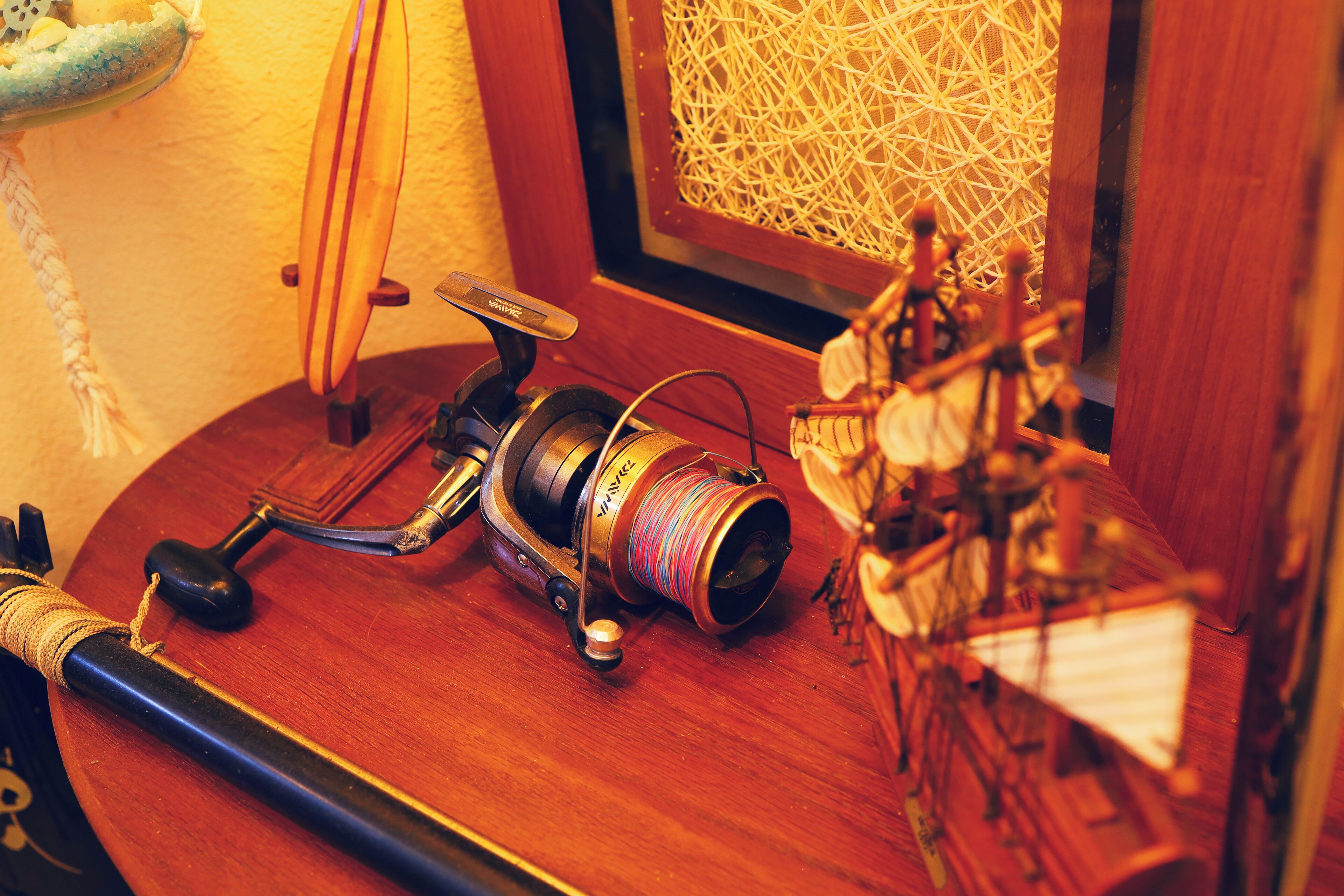 A wooden table with a fishing rod, a reel, and a small model ship.