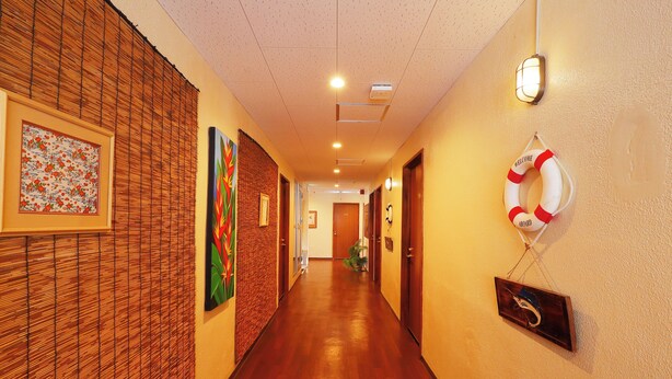 A hotel hallway with wooden flooring, framed artwork, a life preserver decoration, and a welcome sign. - Sazanka (Okinawa)