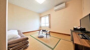 Hotelkamer met tatami matten, een bed, een bureau met stoel, een televisie en een airconditioner.