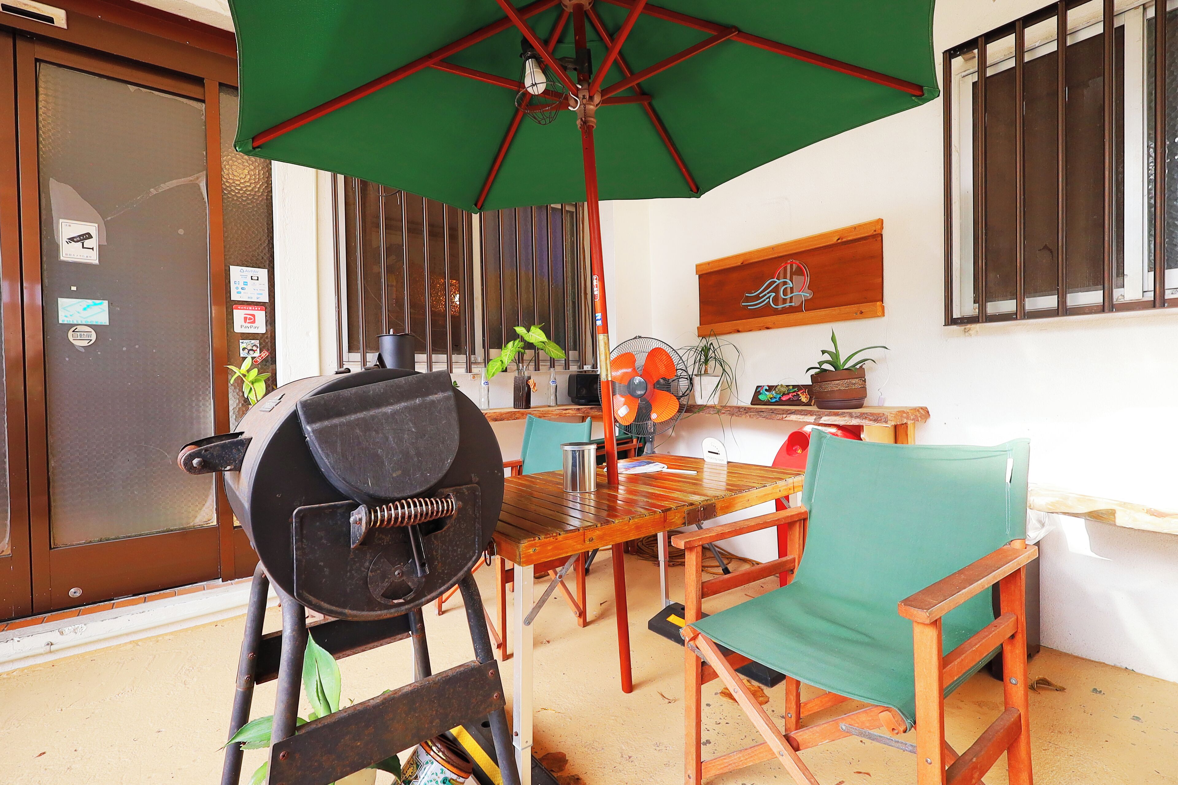 A patio area with a wooden table, a green umbrella, and a barbecue grill.