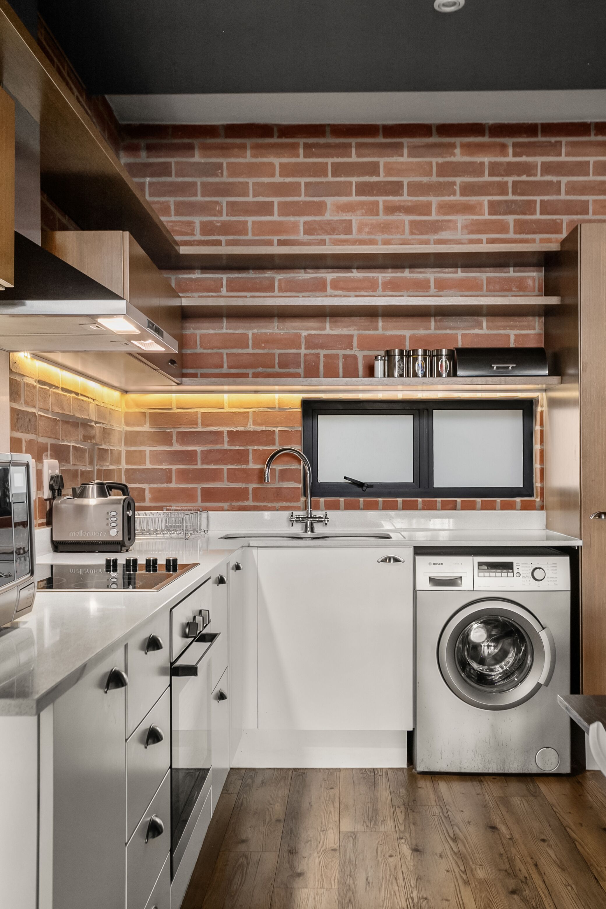 Una cocina moderna con protector mural de ladrillo, electrodomésticos de acero inoxidable y suelo de madera.