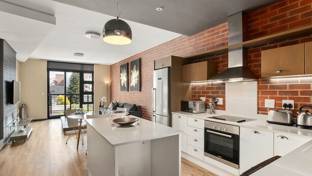A modern kitchen with a central island, stainless steel appliances, and a brick accent wall. - Easy Stay - The Vantage (Johannesburg)