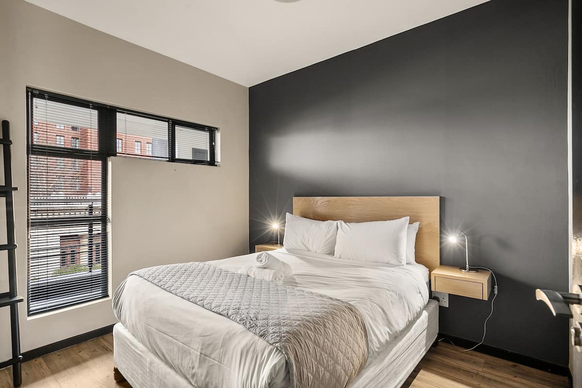 Una cama bien hecha con cabecera, lámparas de noche y una ventana con persianas.