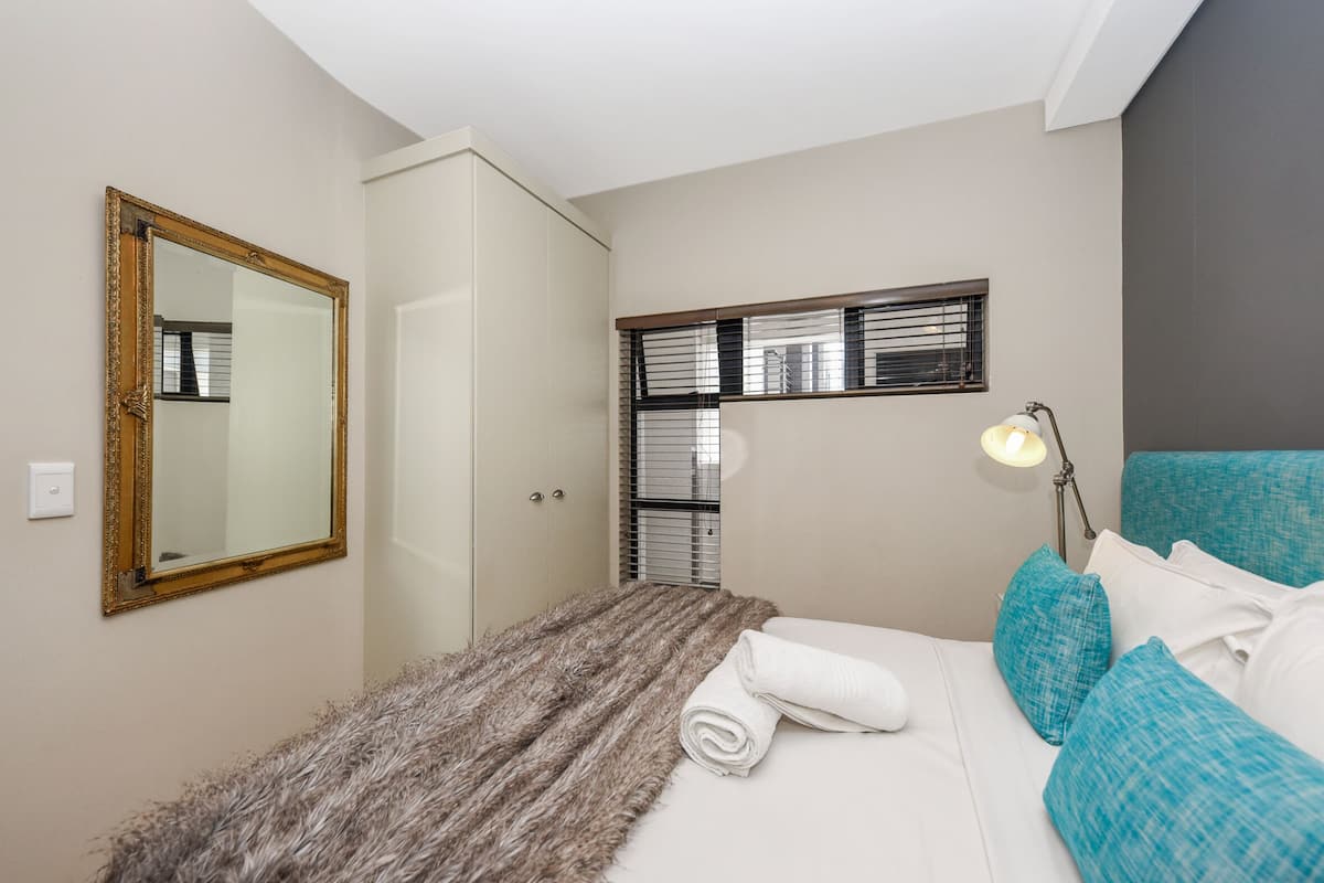 Un dormitorio con cama, espejo, ventana con persianas y lámpara.