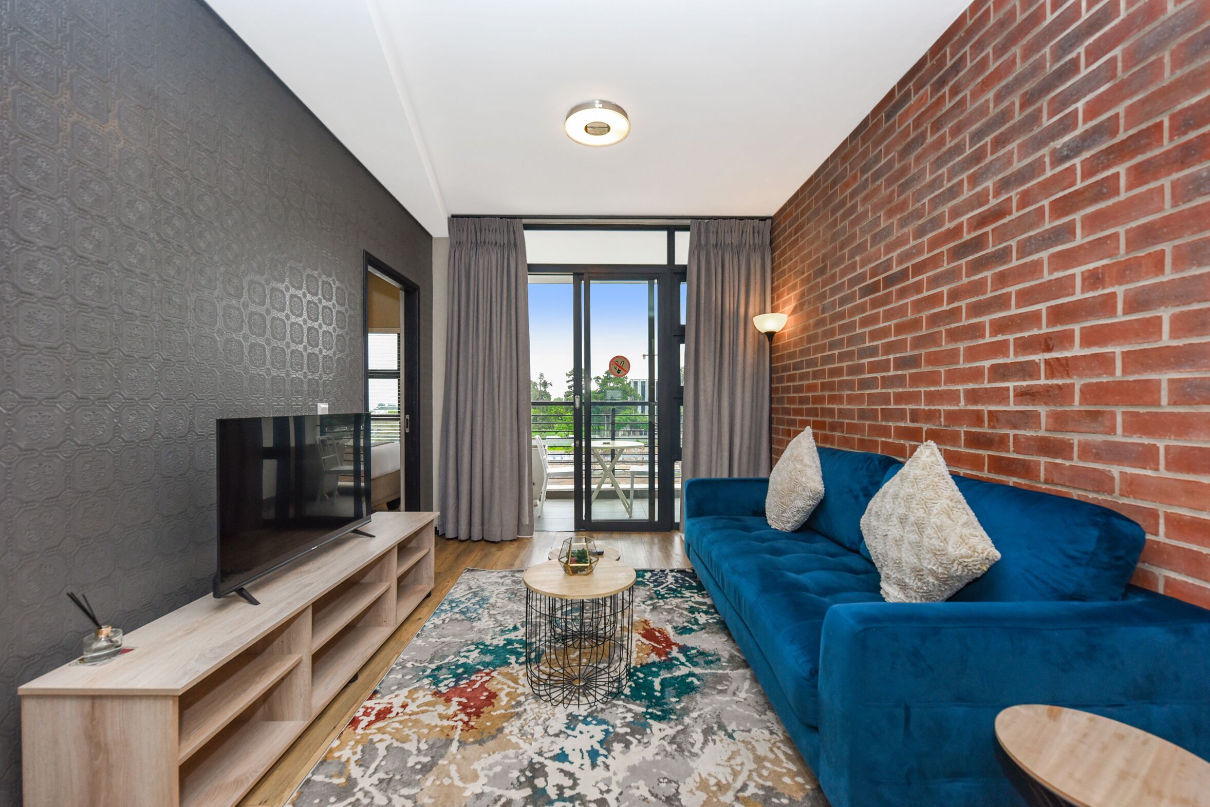 Un salon moderne avec un téléviseur, un canapé bleu et un tapis à motifs.