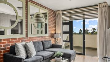 A modern living room with a grey sofa, a glass coffee table with a plant, and a large mirror on a brick wall.