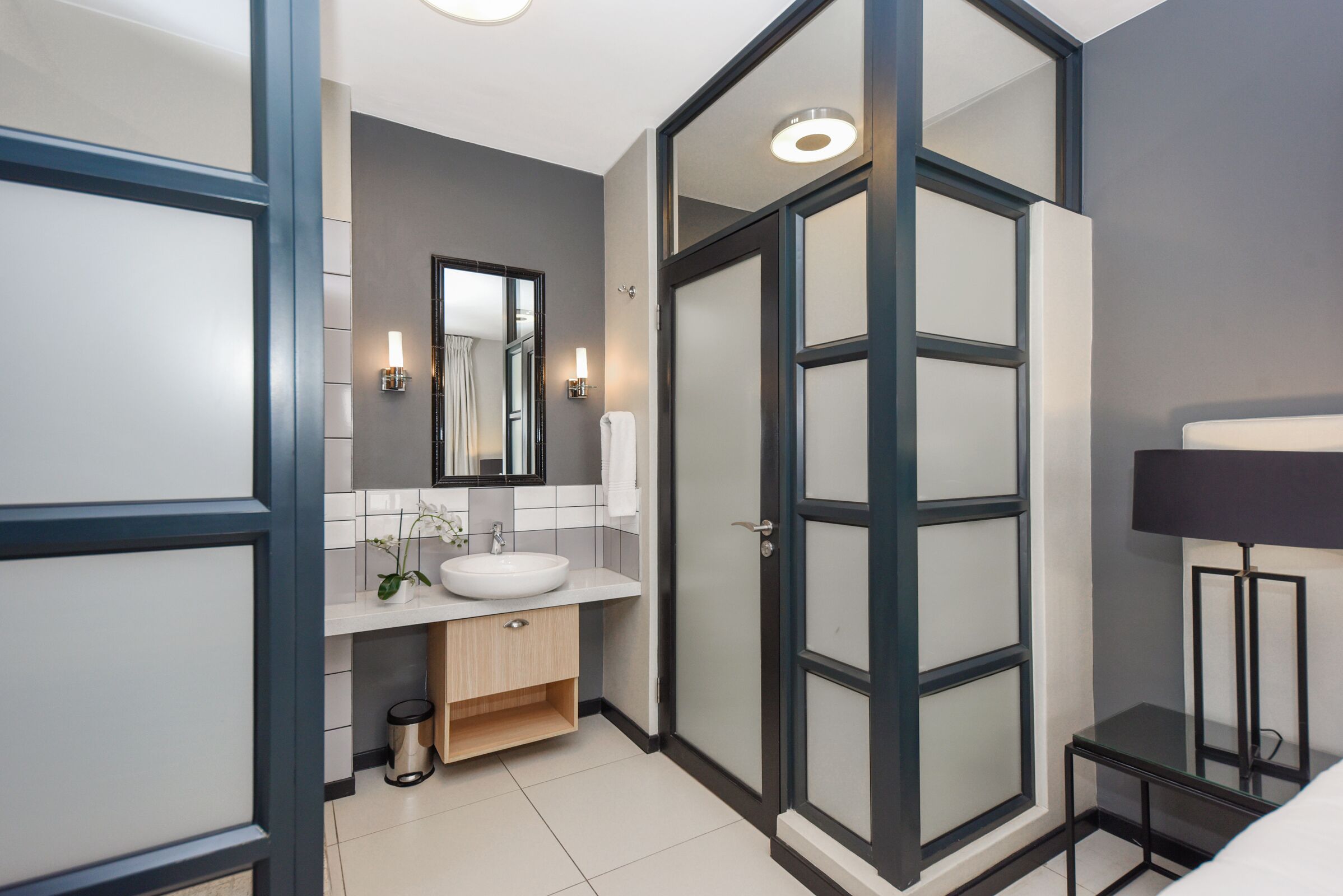 A modern bathroom with a white sink, mirror, and a glass shower enclosure.
