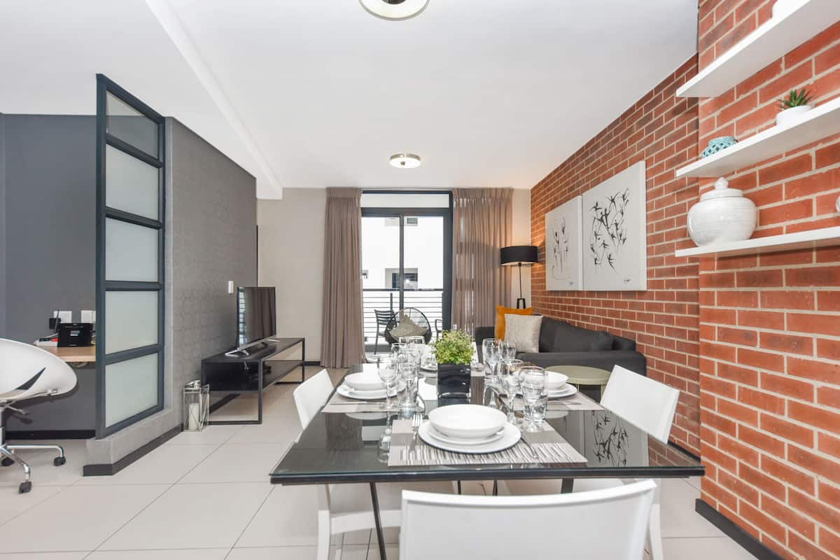 Un comedor moderno con una mesa de vidrio, sillas blancas y una pared de ladrillo decorativa.