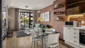 A modern kitchen with a brick wall, white cabinetry, and a microwave. - Easy Stay - The Vantage (Johannesburg)