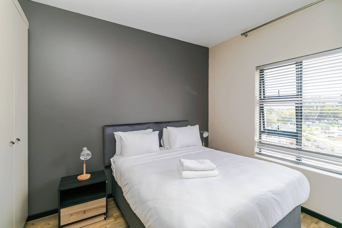 Un dormitorio moderno con cama, mesita de noche y ventana con persianas.