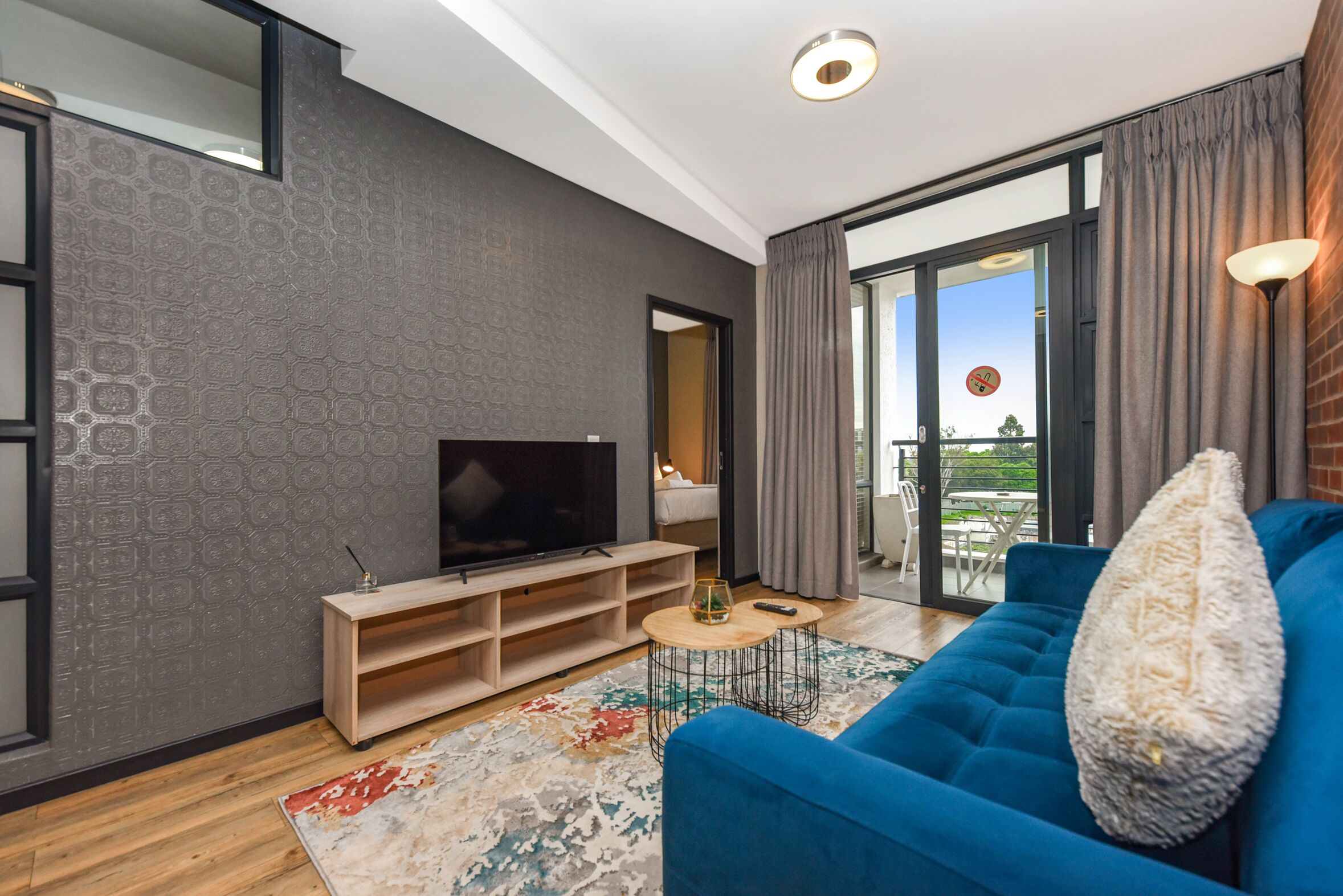 Een moderne woonkamer met een grote flatscreen-tv, een blauwe bank, een houten tv-meubel en een vloerkleed met een patroon.