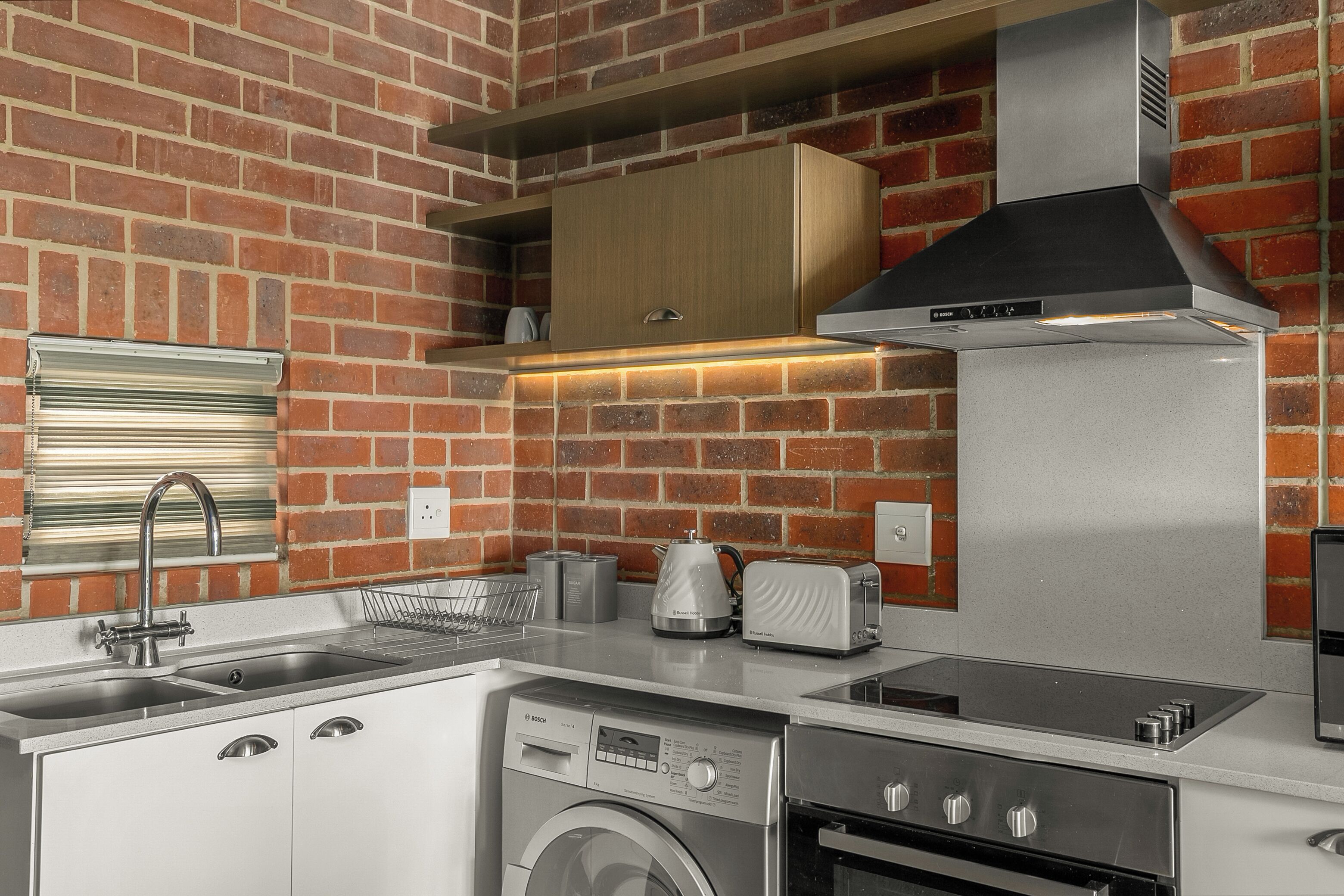 A compact kitchen with a brick wall, stainless steel appliances, and a built-in oven.
