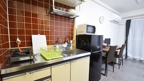 A compact kitchen with a gas stove, microwave, and refrigerator. There is a dining area with a table and chairs. - Yado gh (Sapporo)