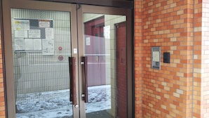 A glass door with a metal handle, a brick wall, and a tiled floor with snow. - Yado gh (Sapporo)