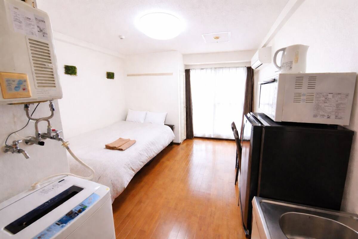Une chambre d’hôtel équipée d’un lit, d’une kitchenette, d’un lavabo et d’une fenêtre avec des rideaux.