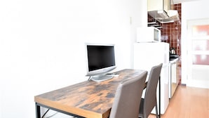 A modern kitchen with a microwave, stove, and oven. There's a dining area with a wooden table and chairs. A clock is mounted on the wall. - Yado gh (Sapporo)