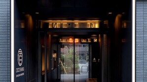 A hotel entrance with a glass door, illuminated by overhead lights, and a sign indicating the hotel name and location. - COCOSHUKU Shinjuku-Hanazono (Tokyo)