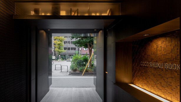 A modern building entrance with a glass door, a bamboo stick, and a brick wall with the text "CO-BOOK". - COCOSHUKU Shinjuku-Hanazono (Tokyo)