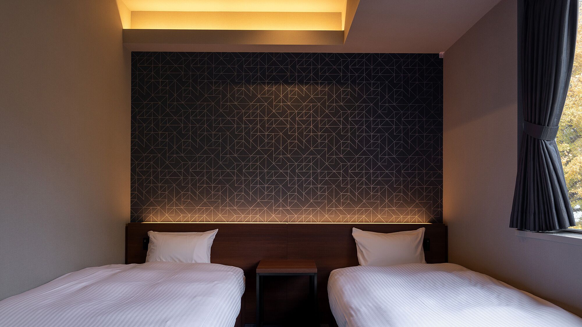 A hotel room with two beds, a geometric patterned wall, and a window with curtains.